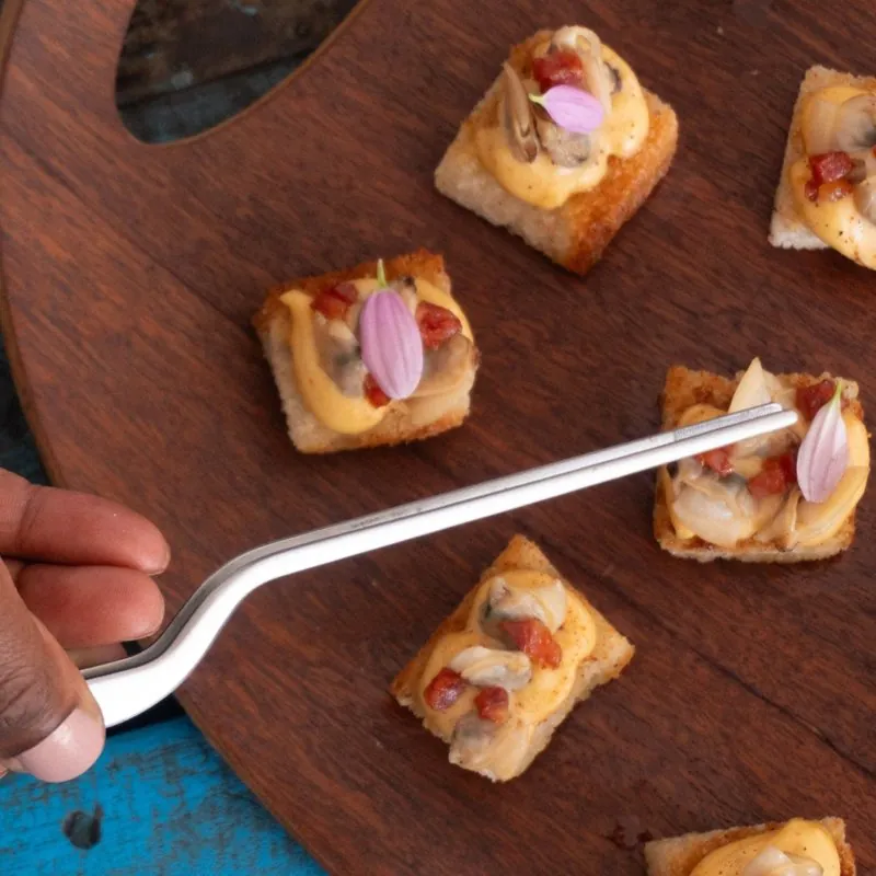 A hand placing a petal with tweezers on clam and chorizo canapés