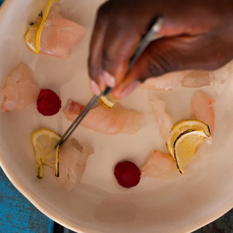 A hand plating raw fish crudo with lemon and raspberries using tweezers
