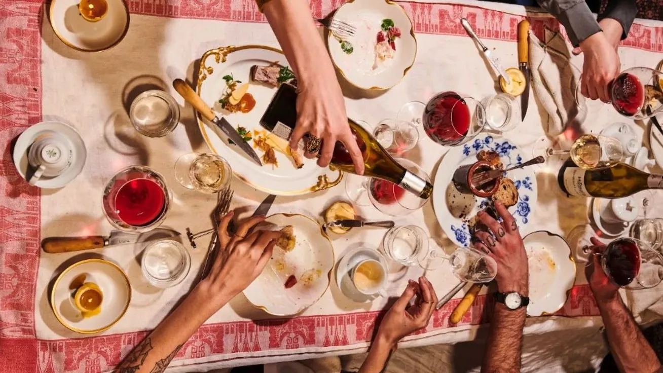 Seen from above, friends around a long table with red wine, plates, bread and a bottle being poured